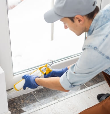 An image of a person using silicone latex caulk on their window frame to prevent bugs from entering. 